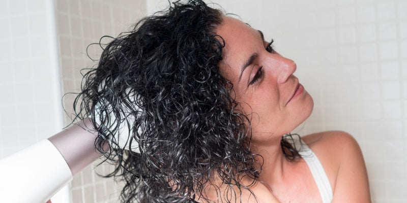 woman with long black curly hair using a diffuser tool on her hair