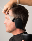 man wearing miss careful black ear covers while coloring hair in a salon