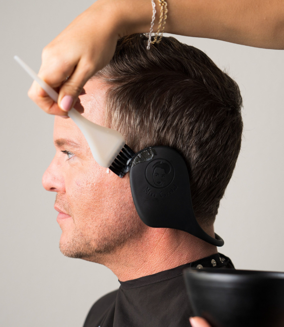 man wearing miss careful black ear covers while coloring hair in a salon