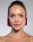 Full frontal photo of a white woman wearing pink color Miss Careful brand of Ear Covers on her ears.
